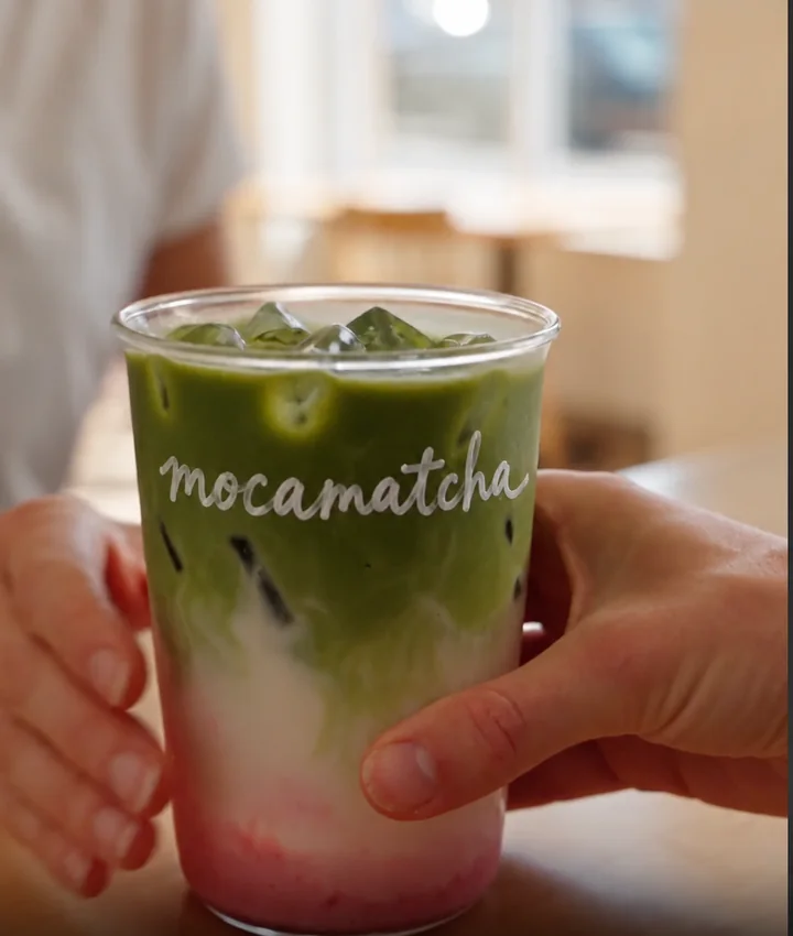 Hands holding an iced Mocamatcha matcha latte with a pink base
